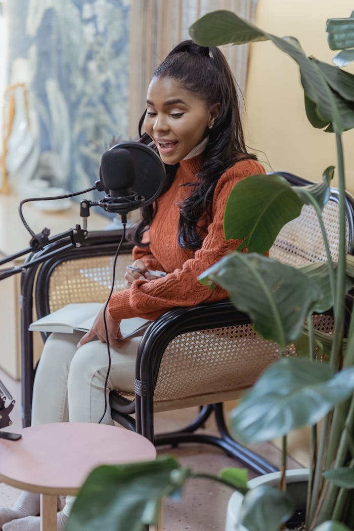 about-us African American woman recording a podcast in an indoor studio with lush green plants.